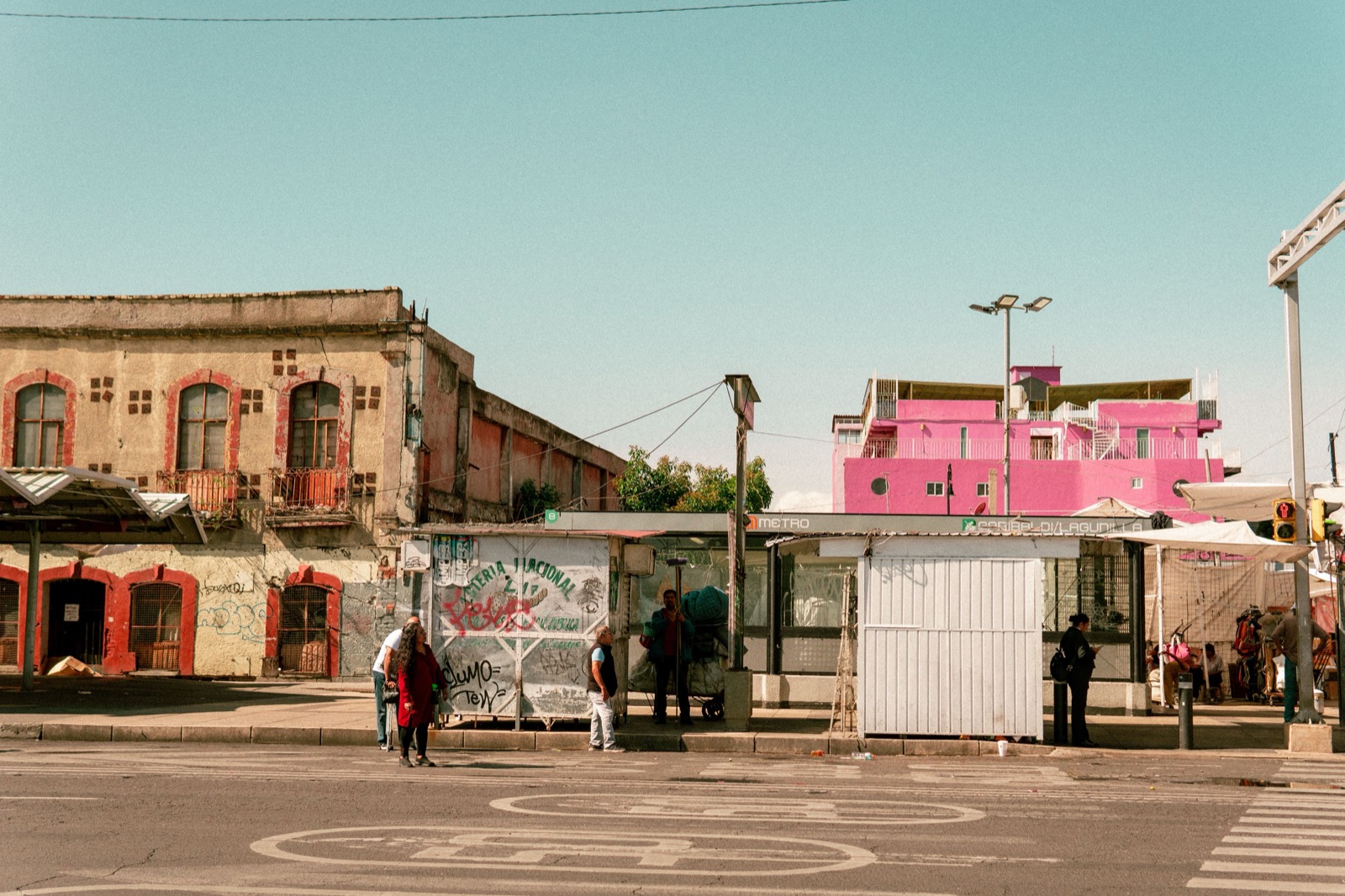 A quiet street with a small shuttered kiosk and a pink building
