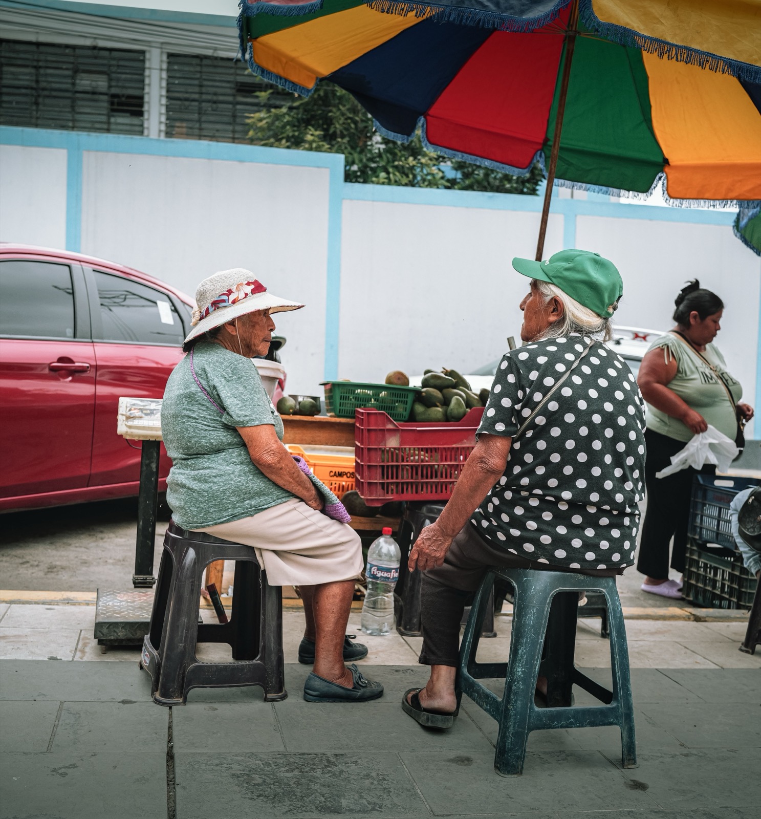 Elders sit and talk beside the stalls of a street market, black and white
