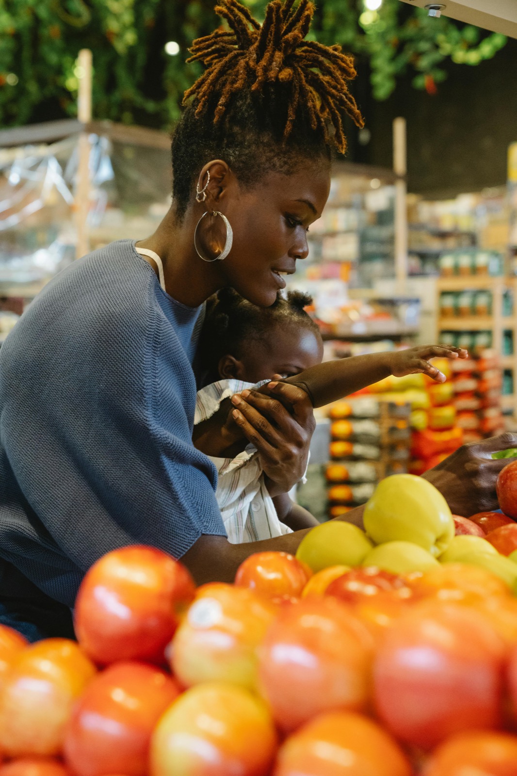 A mother holds her baby at a market stall stacked with tomatoes