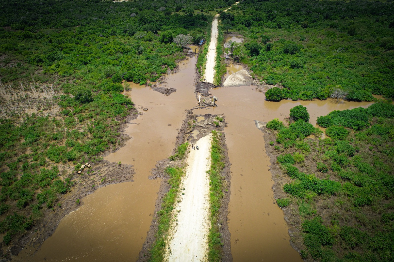 A road cut by floodwater through green land, black and white