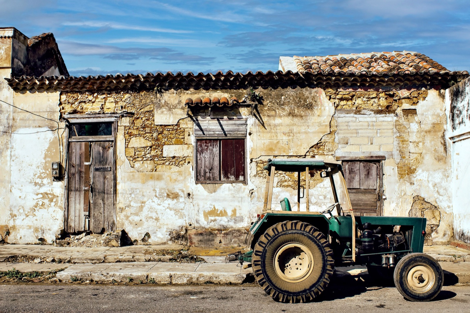 A tractor parked in front of a crumbling house